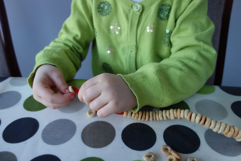 child threading cheerios onto pipecleaner