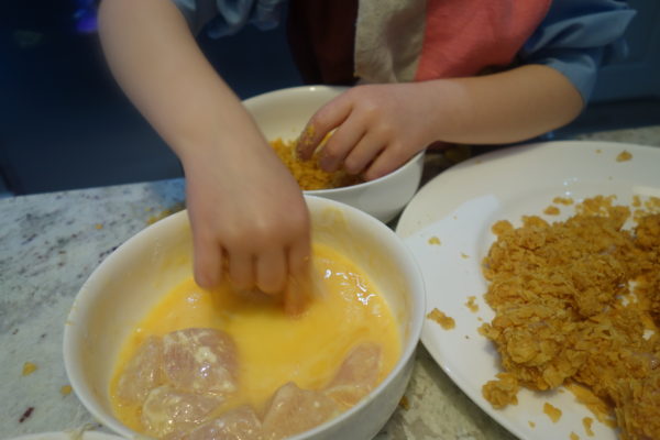 child rolling chicken in coating for homemade chicken nuggets